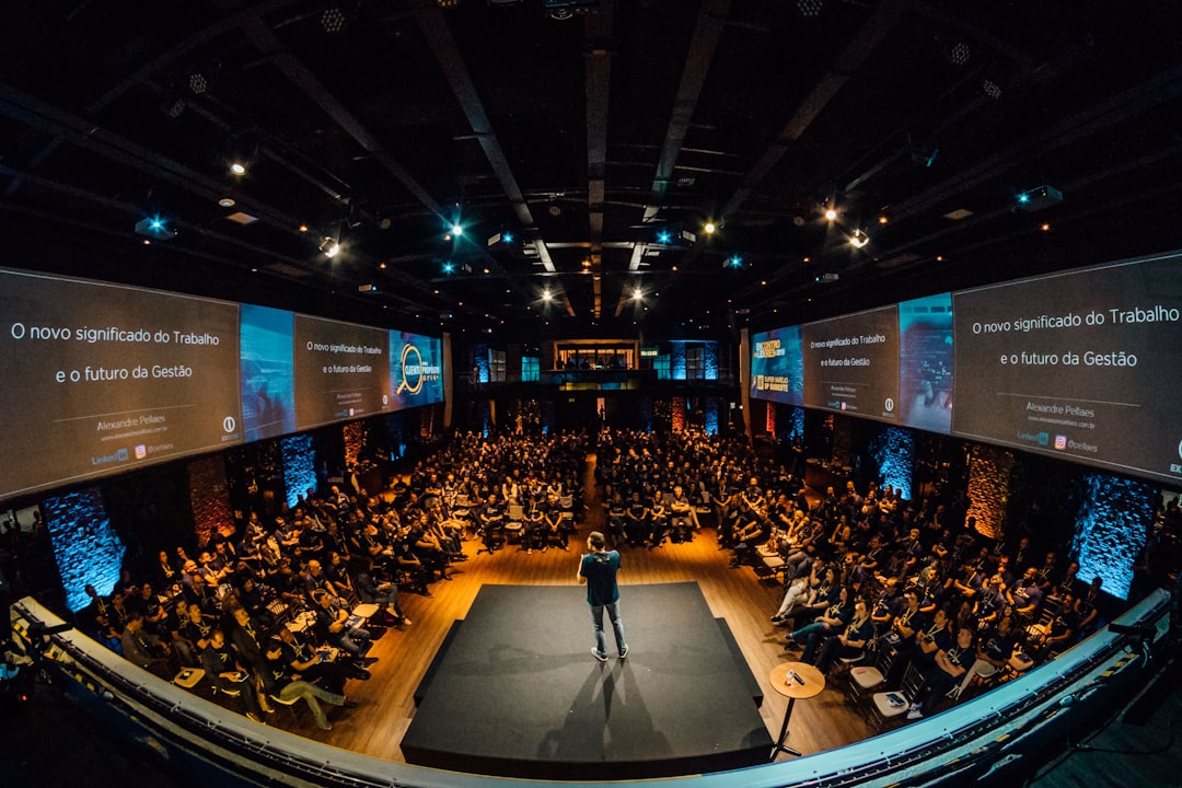 A speaker on a packed stage with screens displaying the talk — what happens when followers become paid appearances.